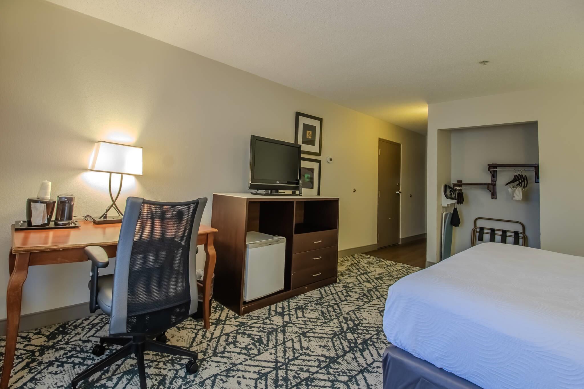 A hotel room with a bed, desk, chair, TV, wardrobe, and a door leading to another room.