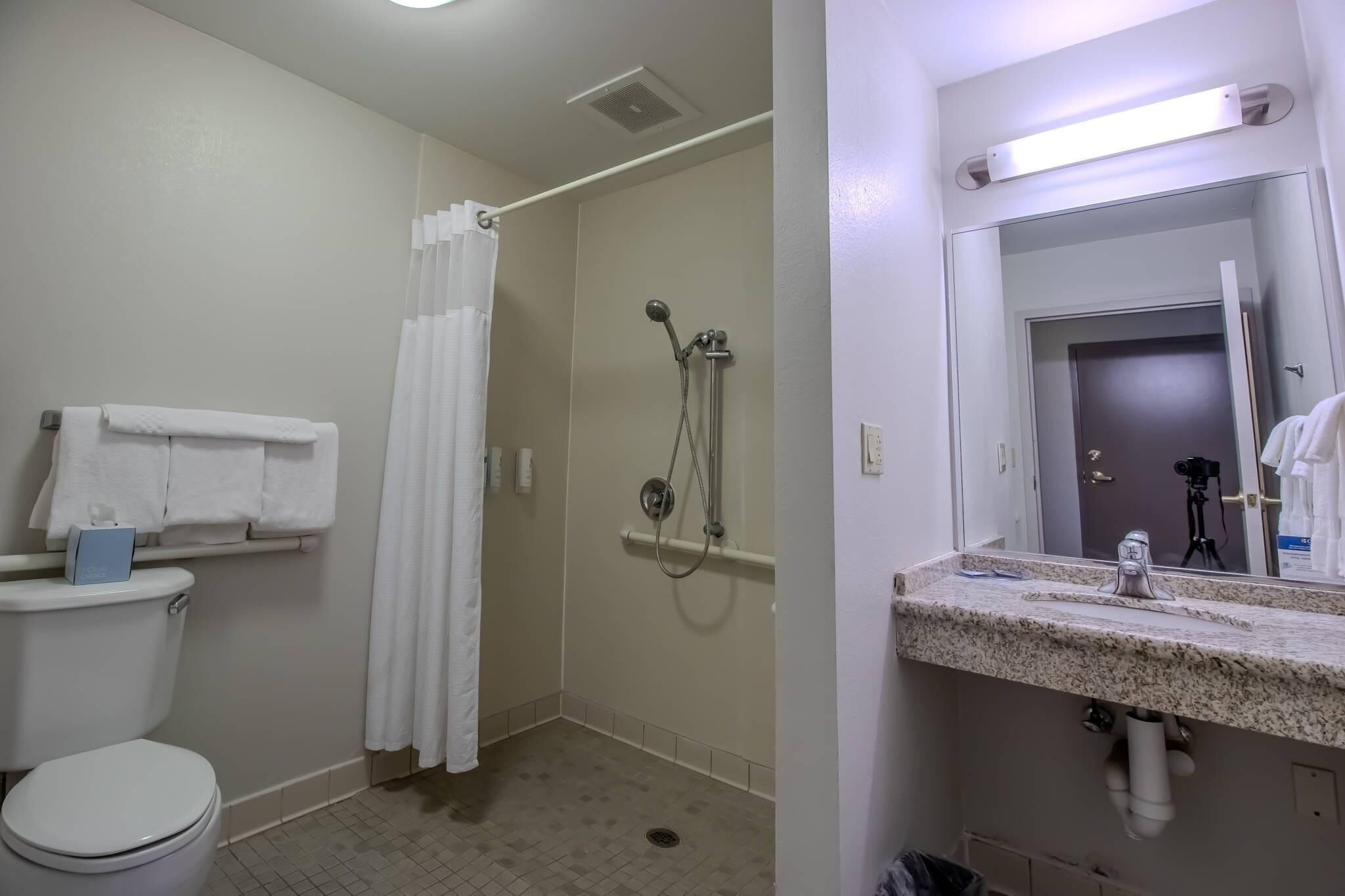 A bathroom with a toilet, shower, and sink with a mirror.