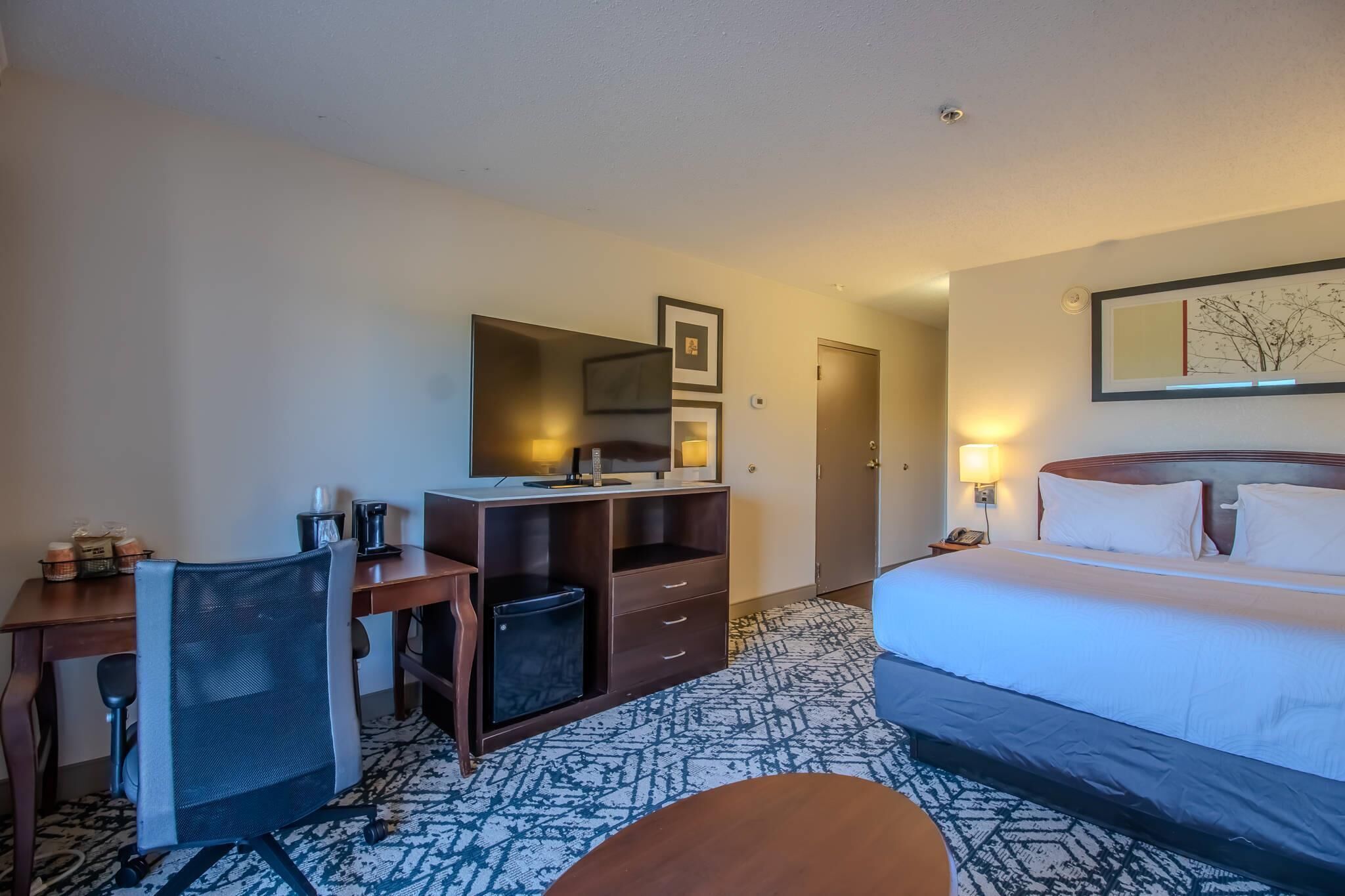 A hotel room with a bed, desk, chair, and a small trash bin.
