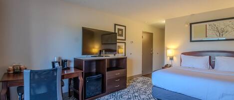 A hotel room with a bed, desk, chair, and a small trash bin.