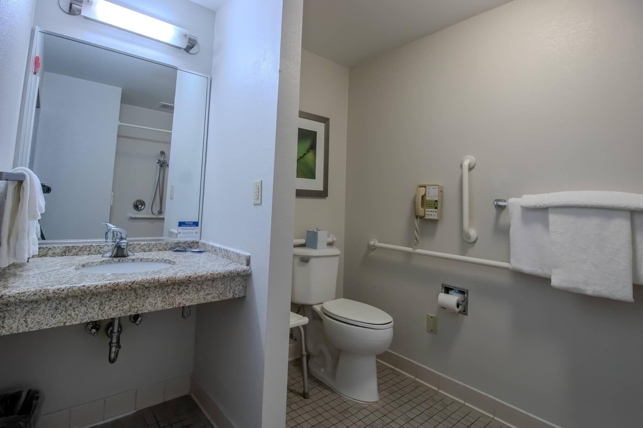 Un baño con lavamanos, espejo, inodoro y barra de apoyo.