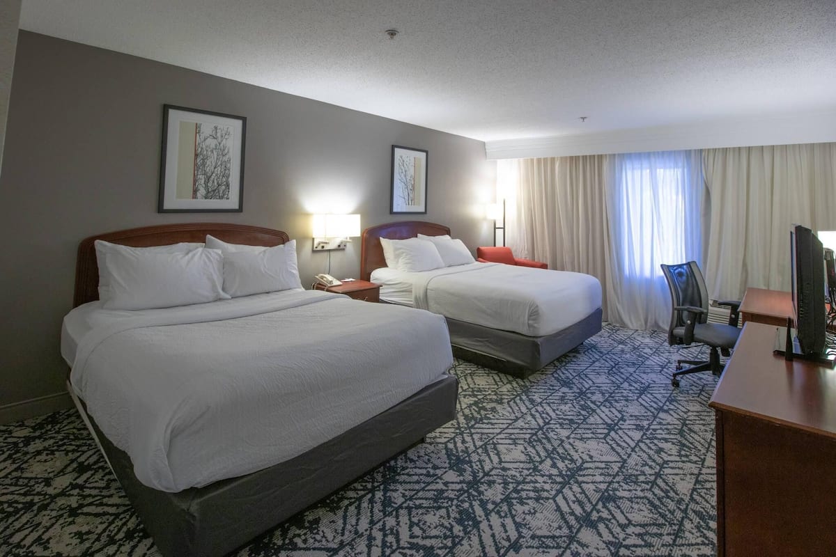 A hotel room with two beds, a desk, a chair, and a TV.