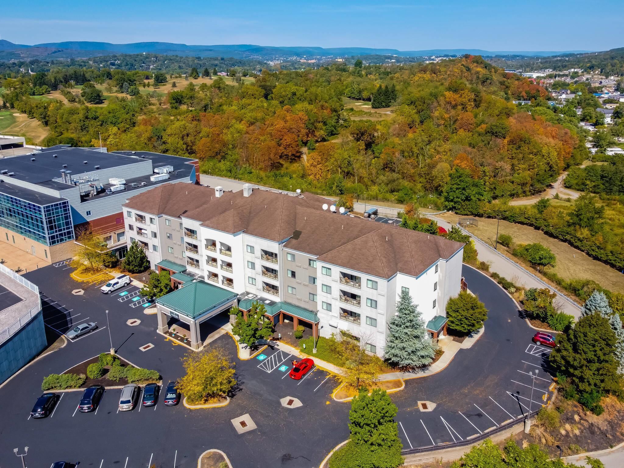 A multi-story hotel with a central courtyard, parking lot, and surrounding greenery.