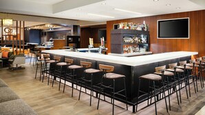 Un área de bar moderna con una barra larga, varios taburetes y una gran variedad de botellas.