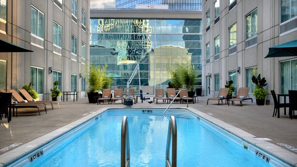 Una piscina interior con agua cristalina, rodeada de sillones de descanso y plantas en macetas, con un edificio moderno al fondo.