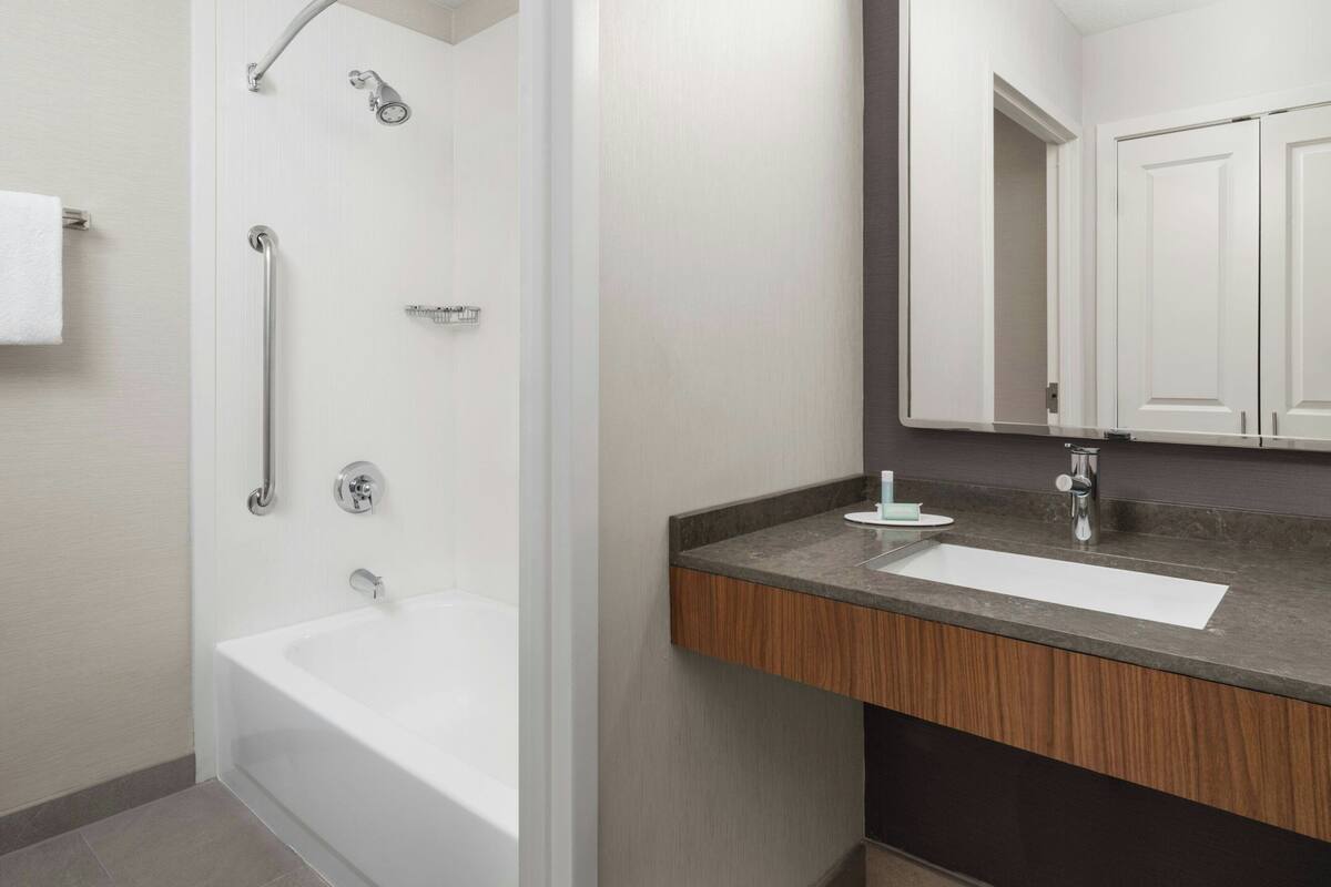 Une salle de bain moderne avec une douche à l’italienne, une baignoire blanche et un meuble-lavabo doté d’un plan de travail en bois.
