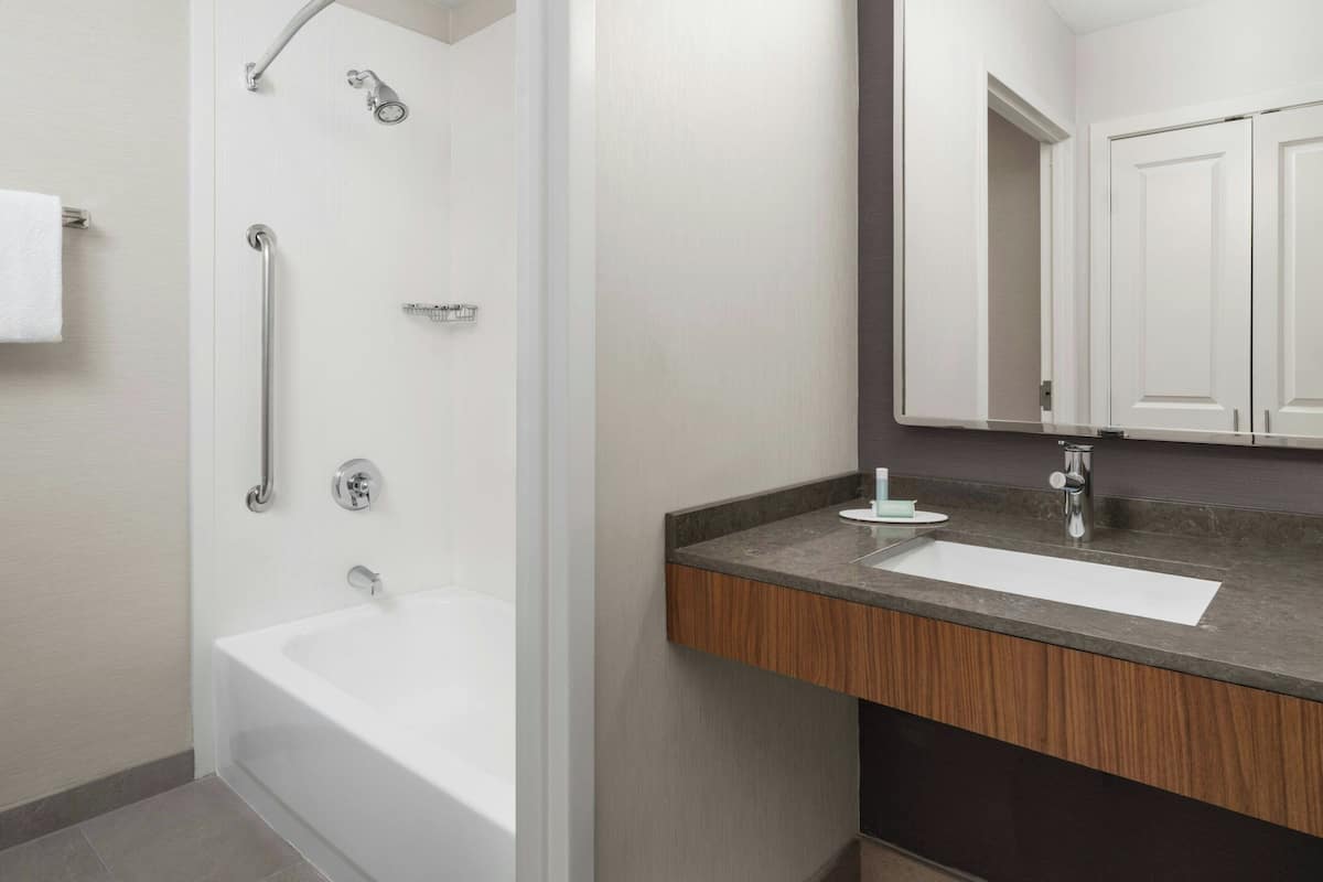 Un baño moderno con cabina de ducha, una bañera blanca y un tocador con encimera de madera.