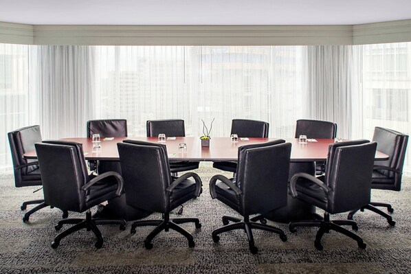 A conference room with a large table, eight black office chairs, and a carpeted floor.