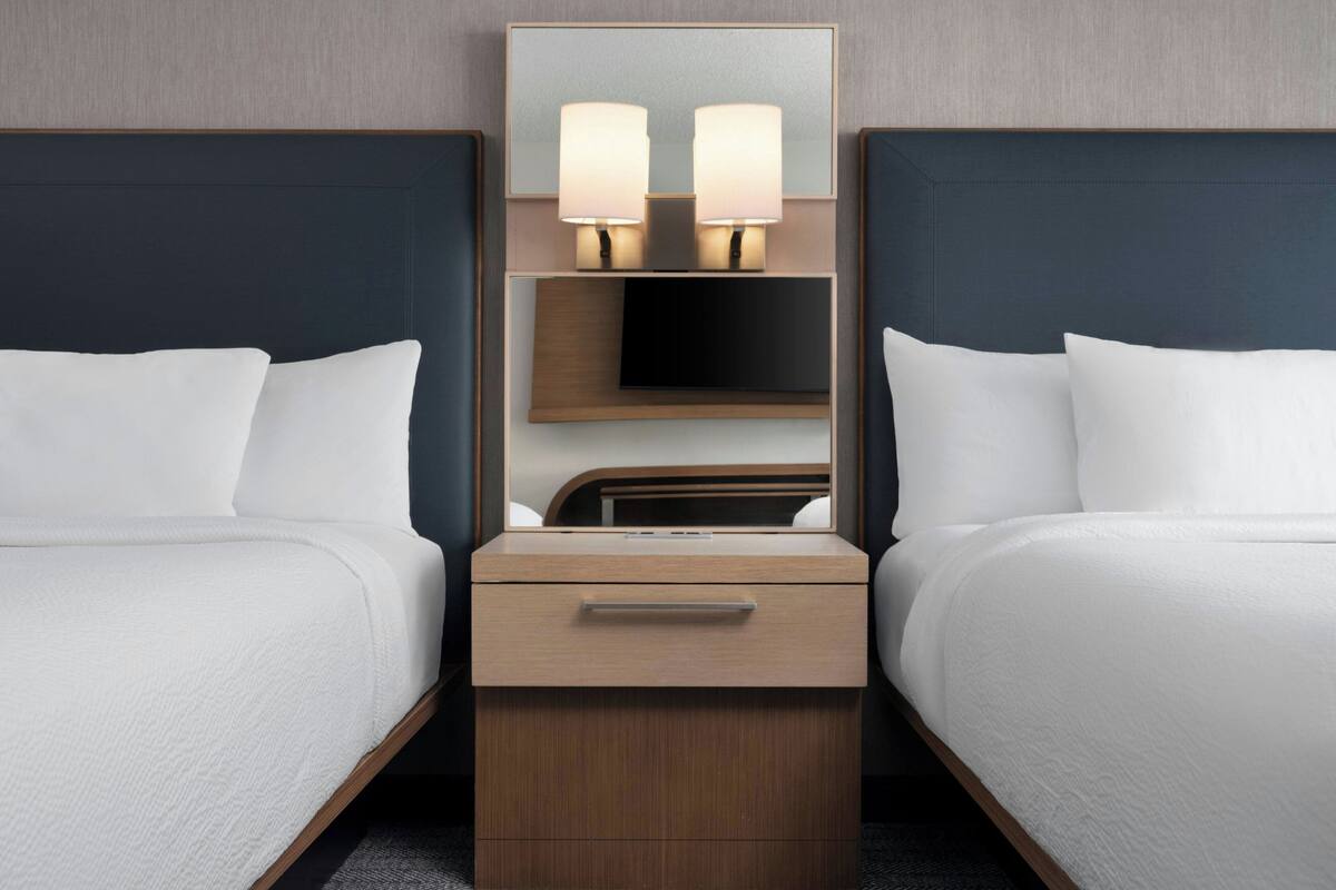 Une chambre d’hôtel avec deux lits, une table de chevet avec une lampe, une télévision et un miroir.