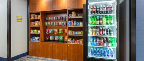 A vending machine stocked with various beverages and snacks, surrounded by wooden cabinets with shelves of packaged goods.
