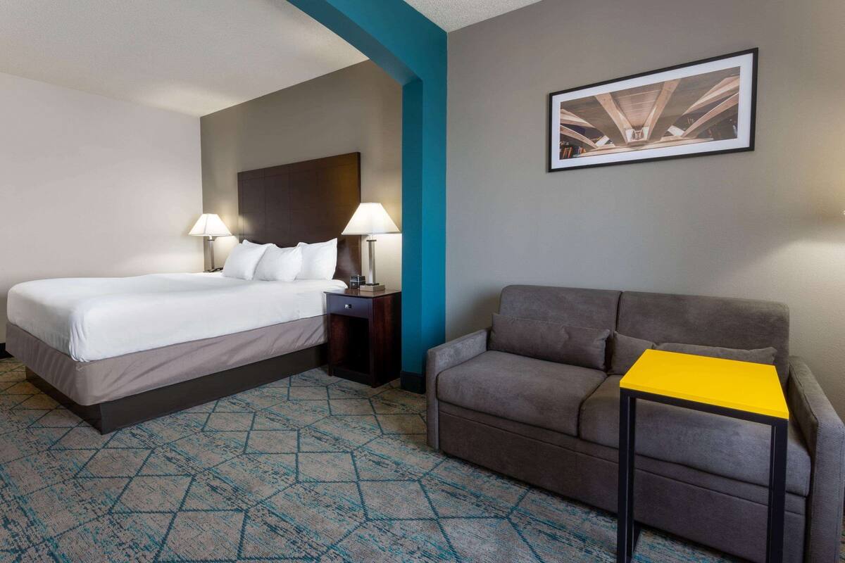 Una habitación de hotel con cama, sofá, una mesita y un cuadro colgado en la pared.
