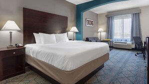 Habitación de hotel con una cama grande, dos mesitas de noche con lámparas, un escritorio, una silla y una ventana con cortinas.