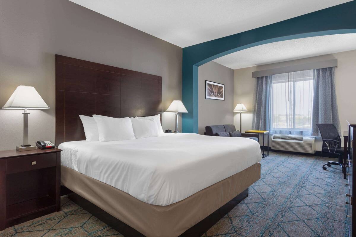 Habitación de hotel con una cama grande, dos mesitas de noche con lámparas, un escritorio, una silla y una ventana con cortinas.