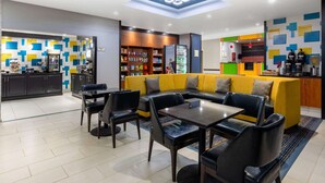 Un moderno vestíbulo de hotel con comedor, un sofá y una zona de cocina con refrigerador y estantes llenos de bocadillos.