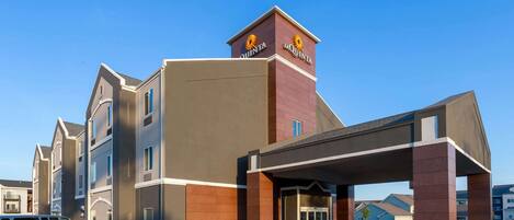 A hotel with a prominent entrance, a parking area, and a clear blue sky.