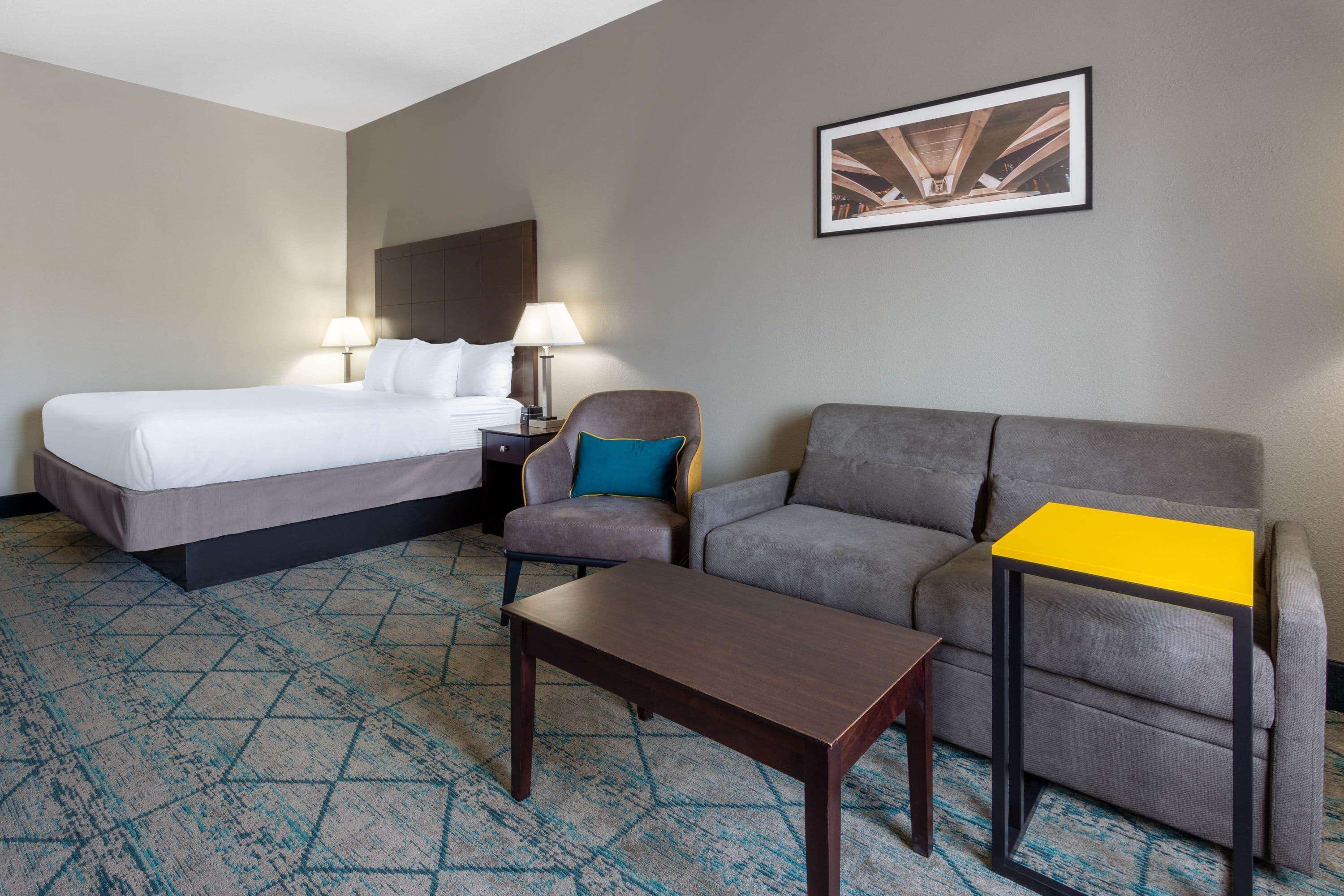 A hotel room with a bed, a sofa, a small table, and a nightstand with lamps.