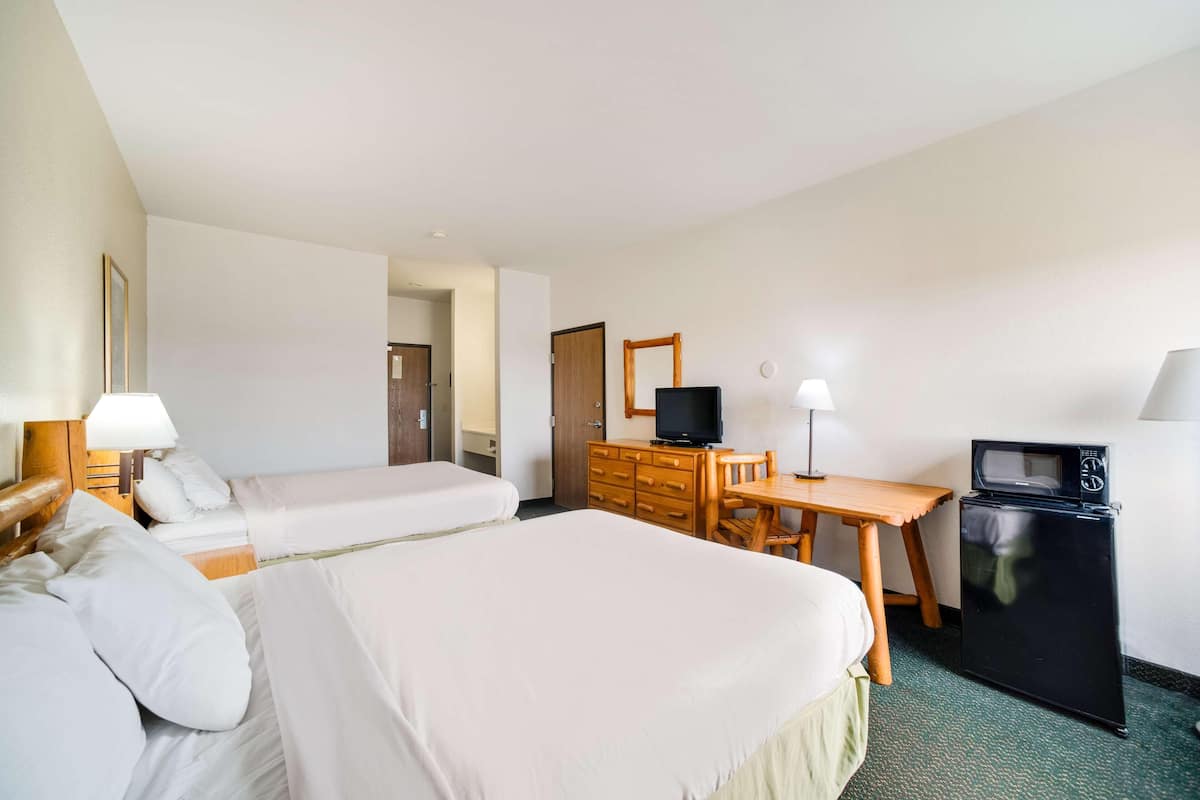 A hotel room with two beds, a desk, a television, and a refrigerator.