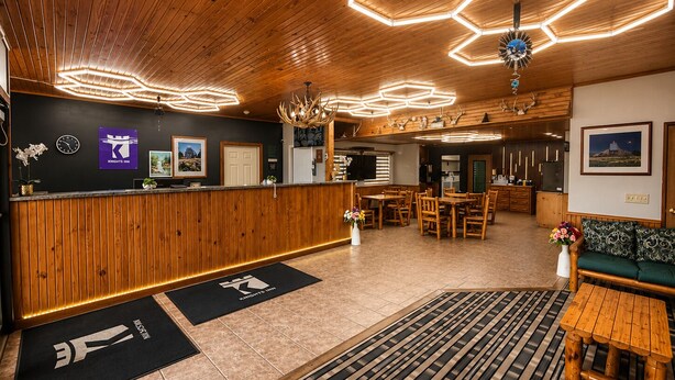 A hotel lobby with a wooden reception desk, hexagonal ceiling lights, a dining area, and a reception desk with a sign. - Knights Inn New Florence (New Florence)