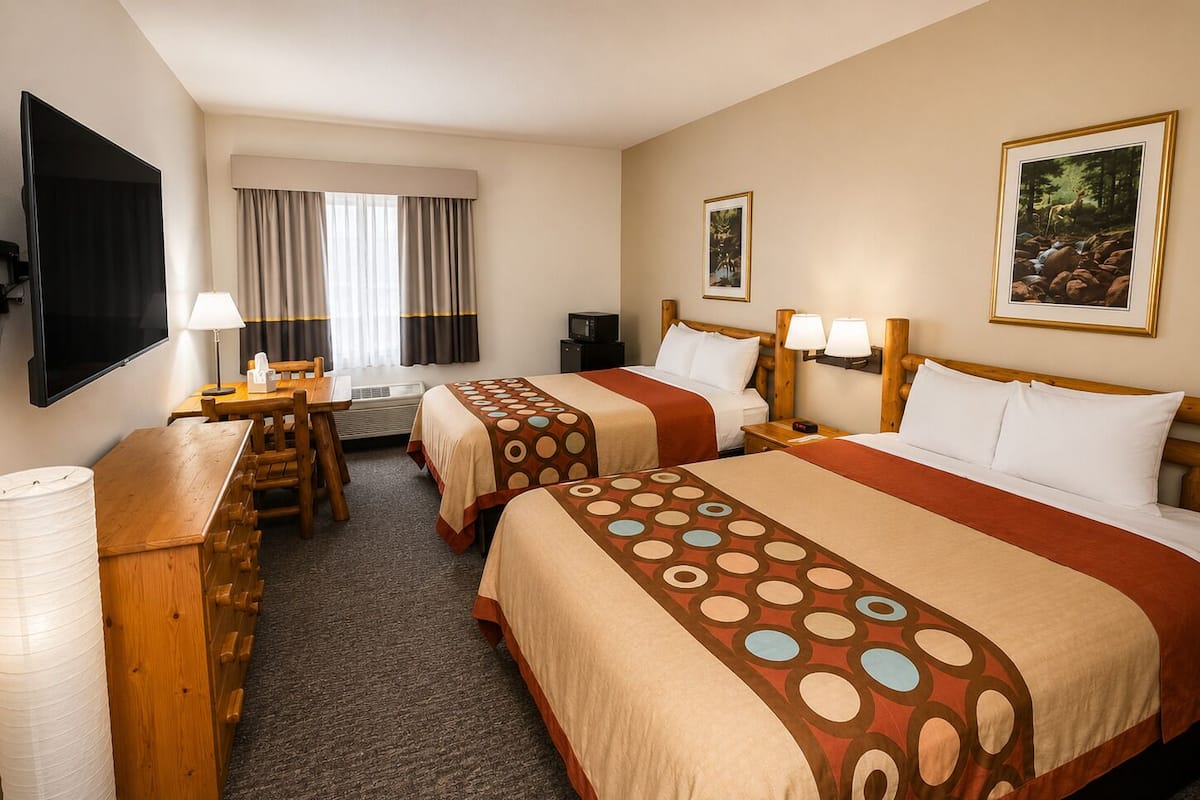 A hotel room with two beds, a desk, a chair, a TV, and a window with curtains.