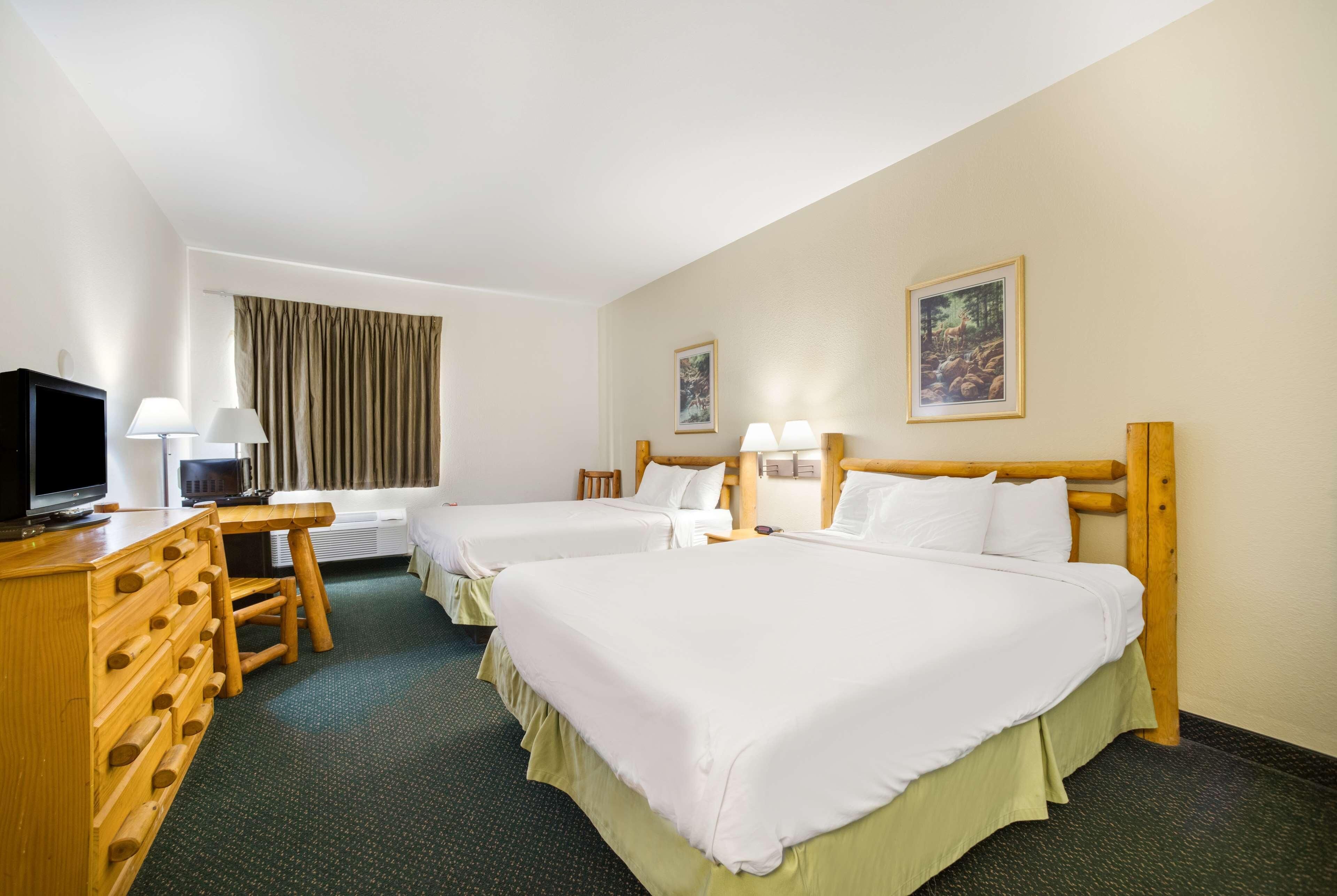 A hotel room with two beds, a desk with a television, and two lamps.
