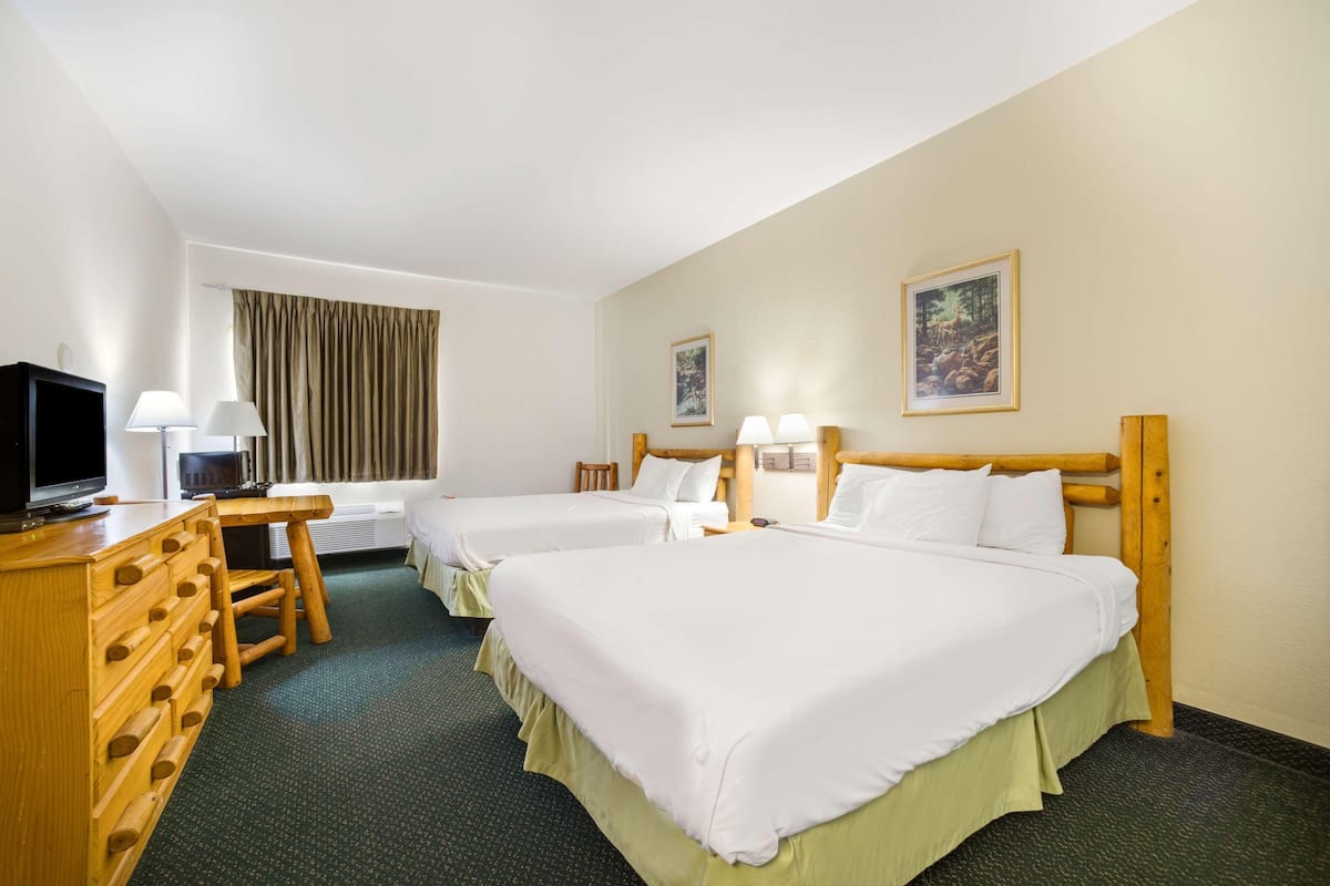 A hotel room with two beds, a desk with a television, and two lamps.