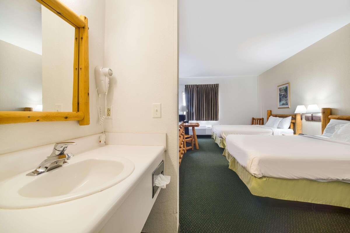 Une chambre d’hôtel avec un grand lavabo blanc, un miroir, deux lits avec du linge de lit blanc, une petite table et une chaise.