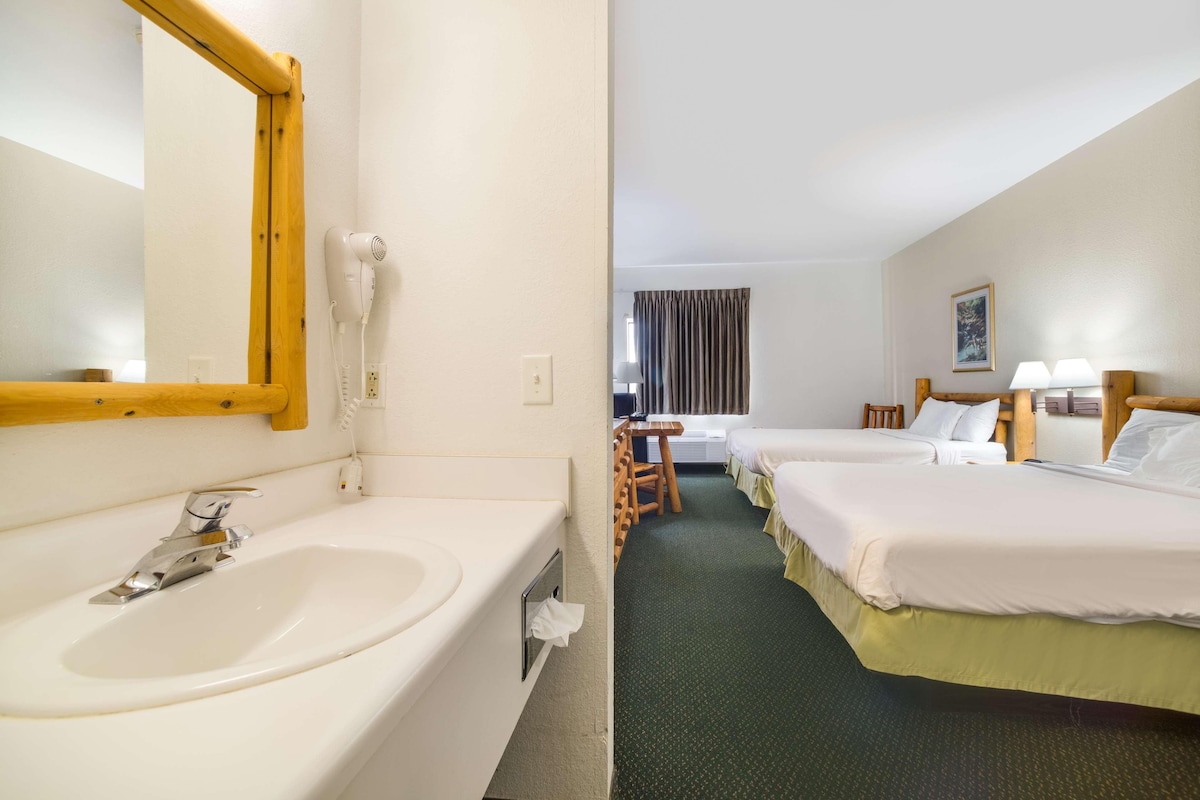 A hotel room with a large white sink, a mirror, two beds with white linens, a small table, and a chair.