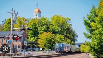 A train crossing with a signal light, a building with a dome, and trees in the background.