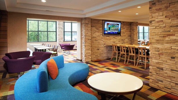 A hotel lobby with a blue sofa, purple chairs, a white table, and a TV mounted on a stone wall.