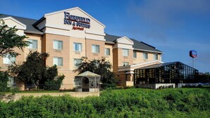 A Fairfield Inn & Suites hotel with a modern glass entrance and a well-maintained garden area.