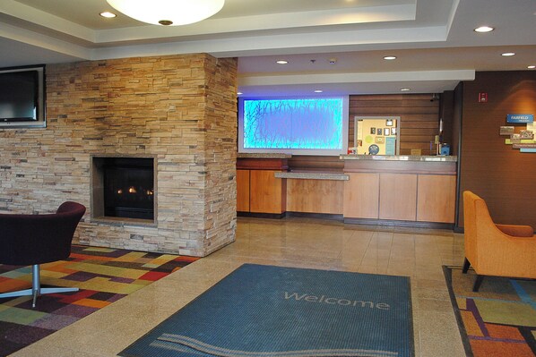 A lobby with a stone fireplace, a reception desk, and a 'Welcome' mat. - Fairfield Inn and Suites by Marriott Indianapolis East (Indianapolis)