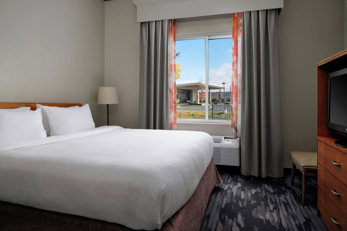 Une chambre d’hôtel avec un grand lit, une télévision, un bureau et une fenêtre avec des rideaux.