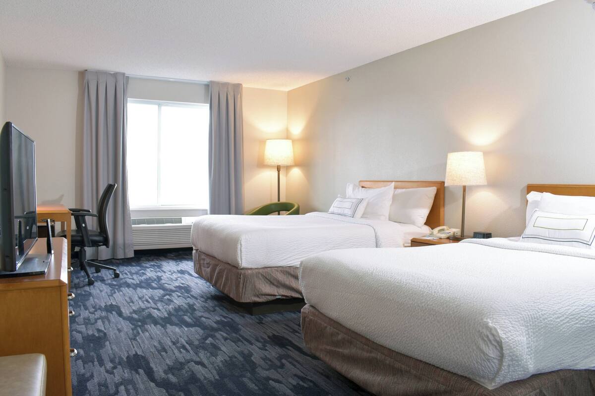 Une chambre d’hôtel avec deux lits, un bureau avec un ordinateur, une chaise et un téléviseur.