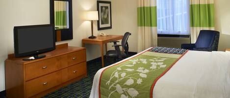 A hotel room with a bed, a desk, a chair, a television, a dresser, a lamp, and a window with curtains.