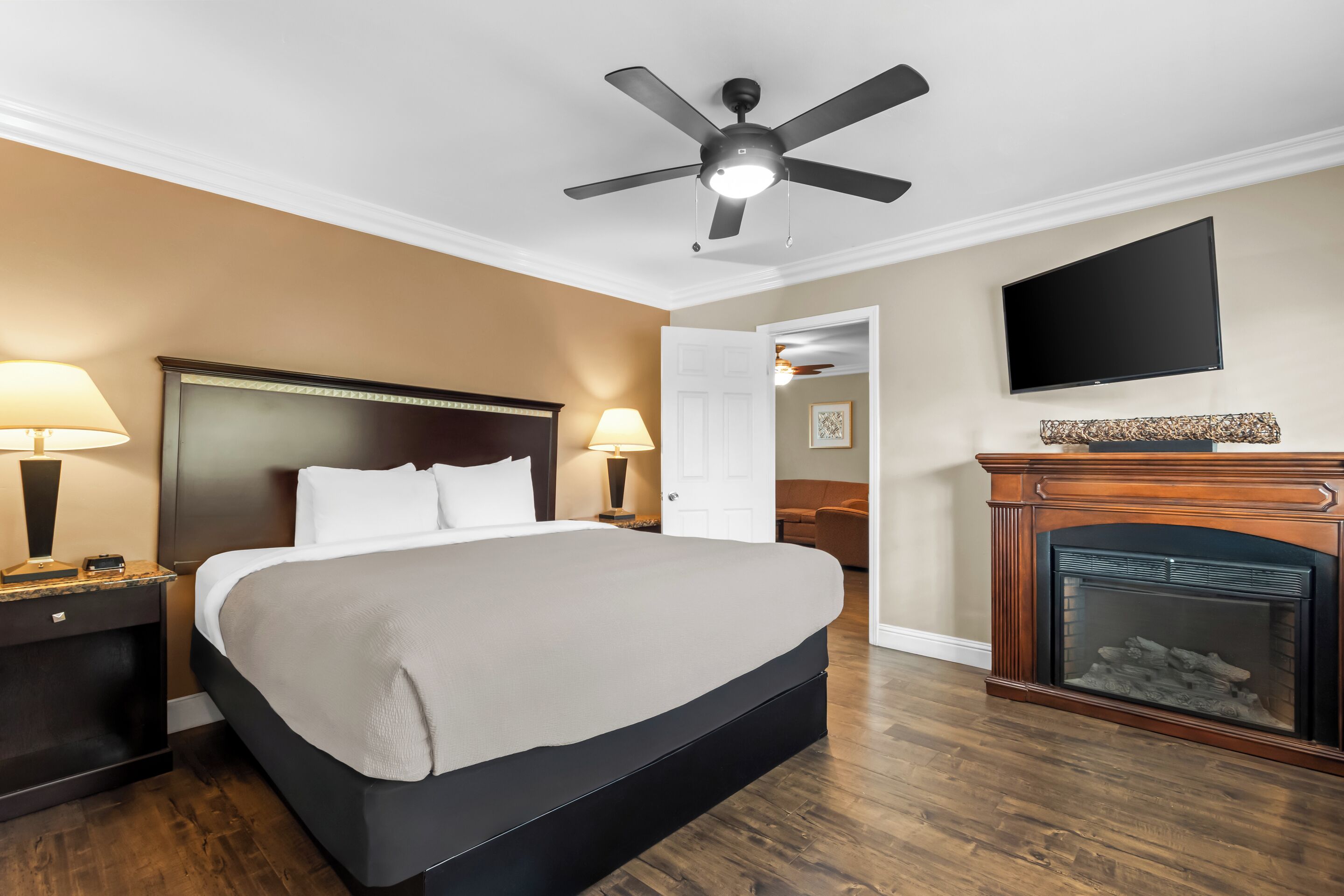 Ein Hotelzimmer mit Bett, Nachttischlampen, Deckenventilator, Fernseher und Kamin.