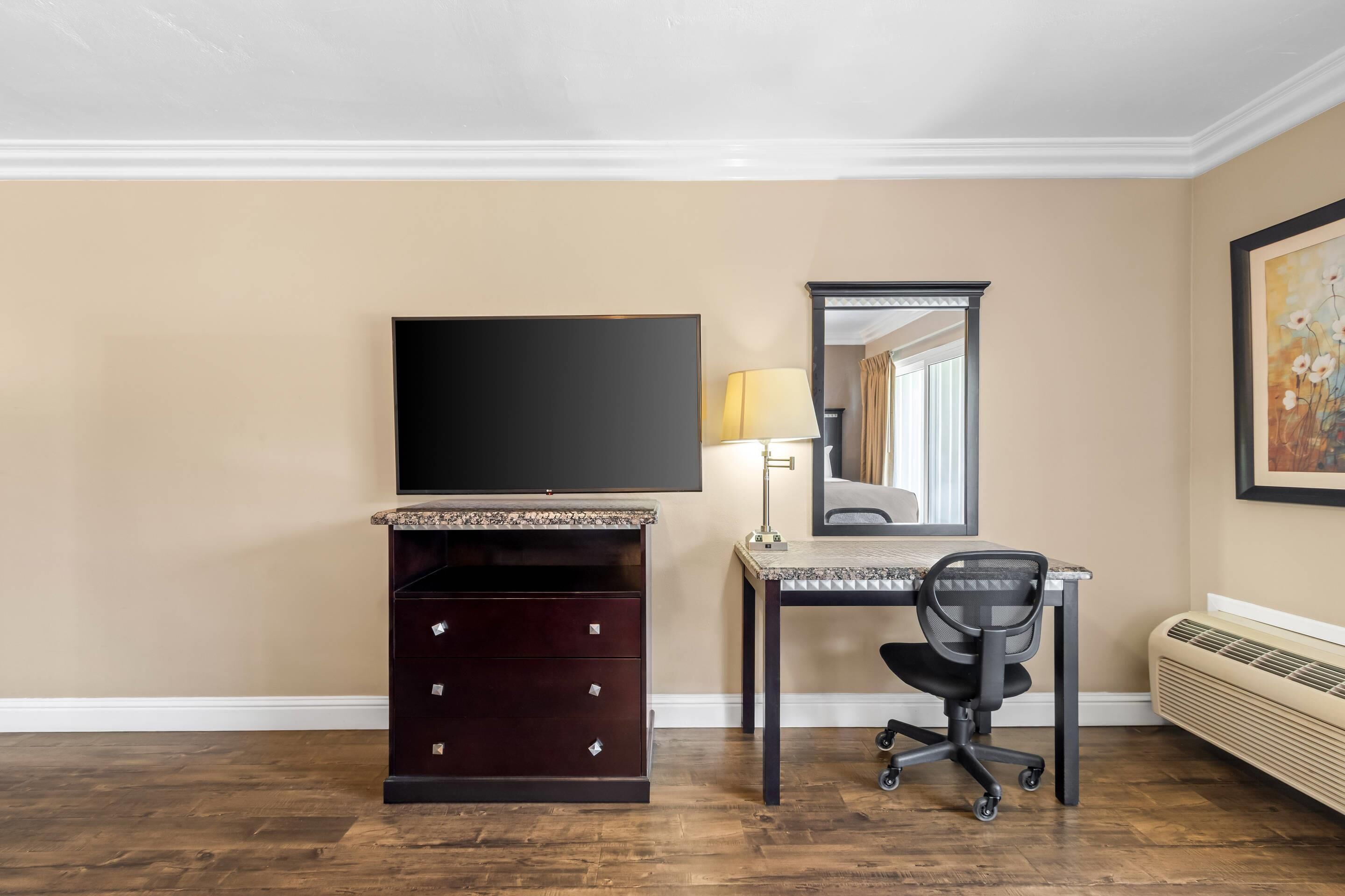 Habitación de hotel con televisión de pantalla plana, escritorio con lámpara, silla, cómoda y radiador.