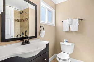 Un baño con un lavamanos blanco, grifo negro, paredes color beige y un inodoro blanco, además de una ventana.