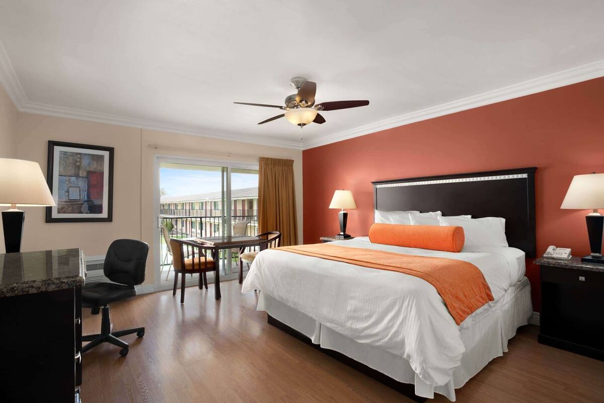 A hotel room with a bed, desk, chair, and a balcony view.