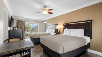 Una habitación de hotel con cama, escritorio, silla, televisor, ventilador de techo y ventana.