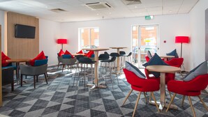 A modern lounge area with multiple seating options, including round tables and chairs, and a patterned floor. - Holiday Inn Express Southampton - West by IHG (Southampton)