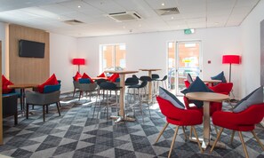 A modern lounge area with multiple seating options, including round tables and chairs, and a patterned floor. - Holiday Inn Express Southampton - West by IHG (Southampton)