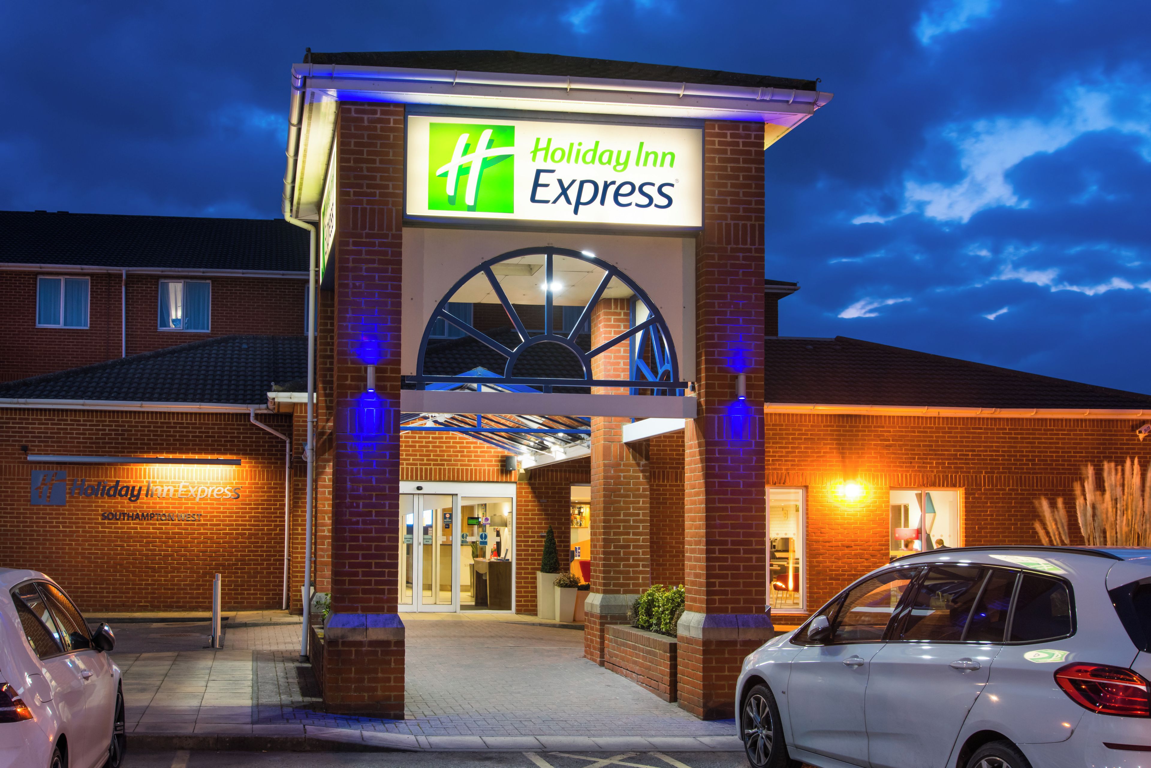Edificio Holiday Inn Express con una entrada destacada, un área de estacionamiento y cielo despejado.