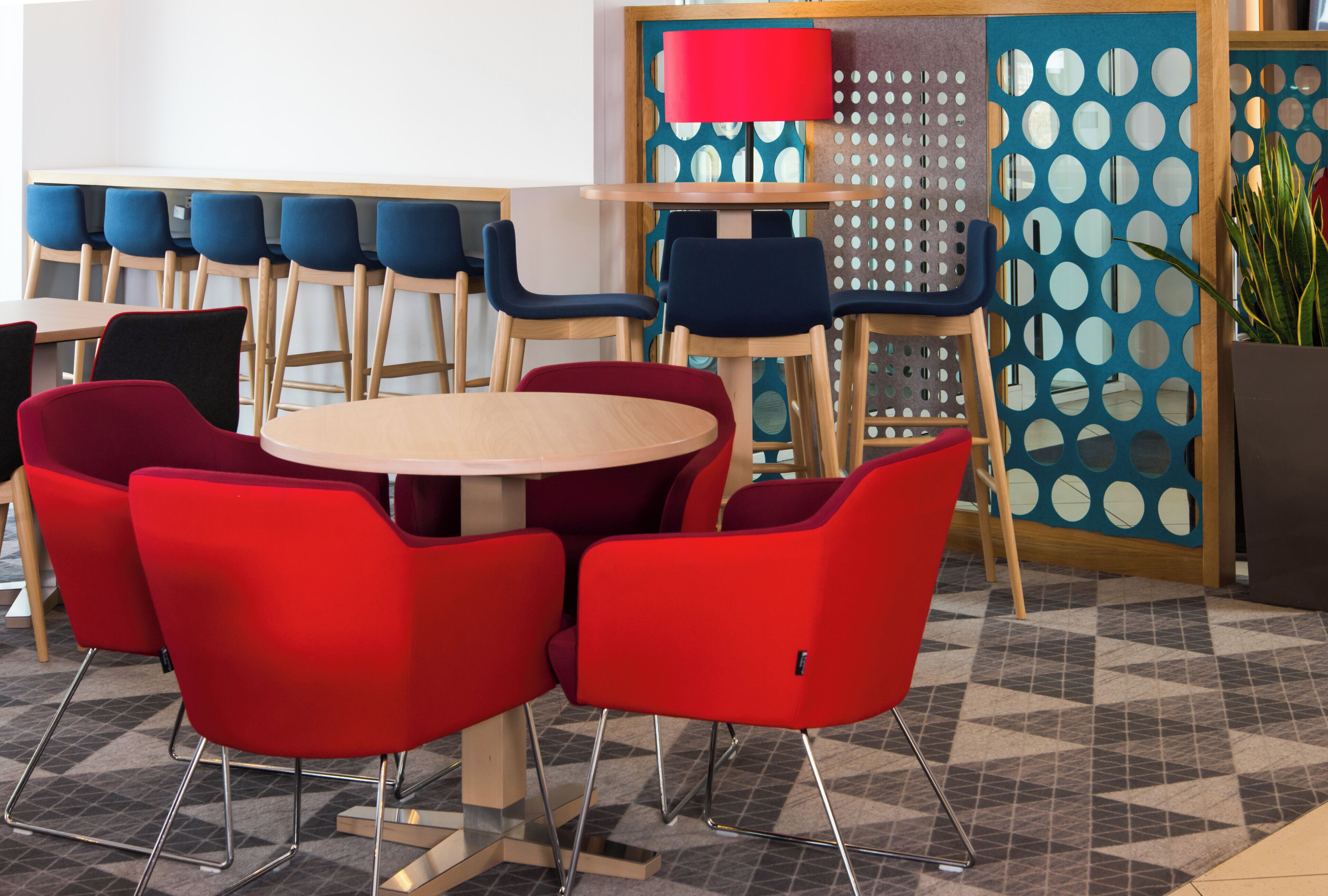 A modern dining area with round tables and chairs, a patterned wall, and a potted plant.