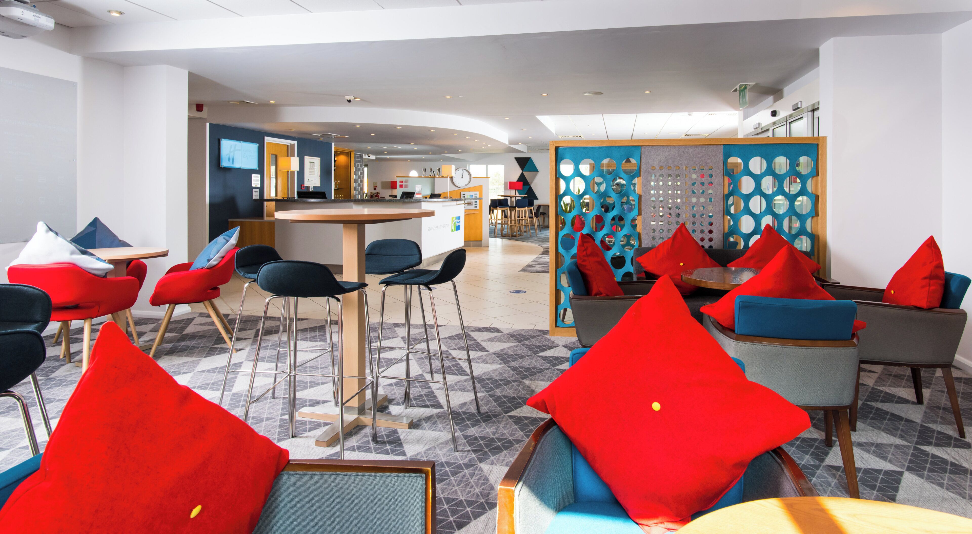 A modern hotel lobby with a bar area, seating arrangements, and a decorative wall.