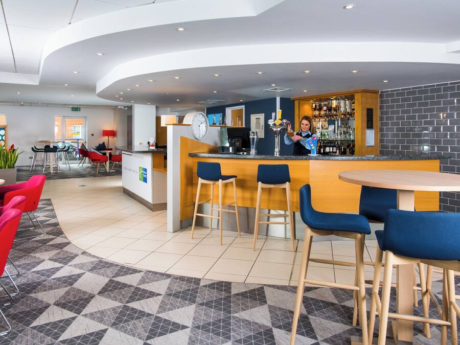 Uma área de bar moderna, com balcão, banquetas e um espaço de estar com mesas e cadeiras.