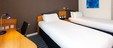 Een hotelkamer met twee bedden, een bureau, een lamp en een blauw abstract schilderij aan de muur.