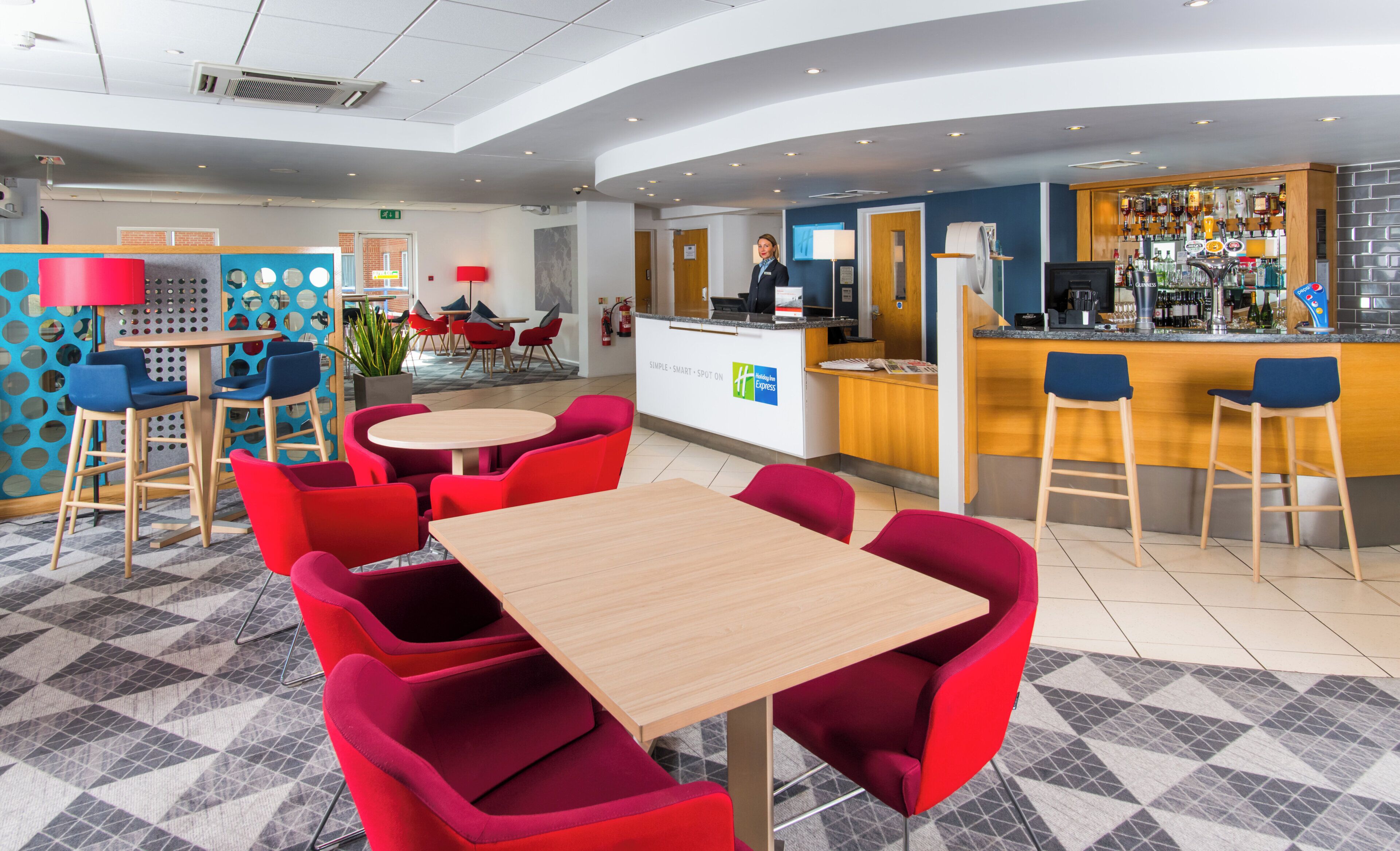 A hotel lobby with a bar area, red seating, and a reception desk.