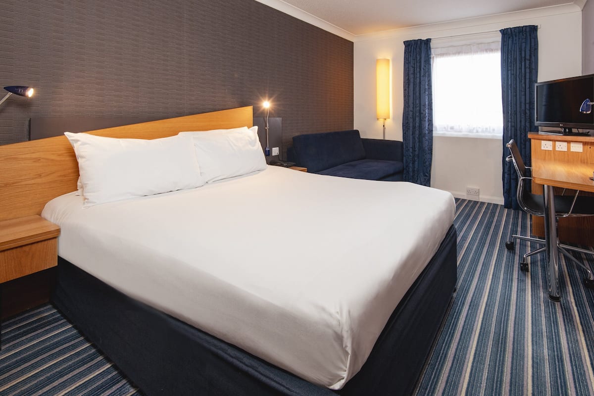 A hotel room with a large bed, a desk with a computer, a chair, and a TV.