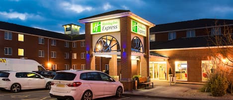 Ett Holiday Inn Express-hotell med en parkeringsplats, tydligt markerade parkeringsplatser för funktionshindrade och en fasad av tegel.
