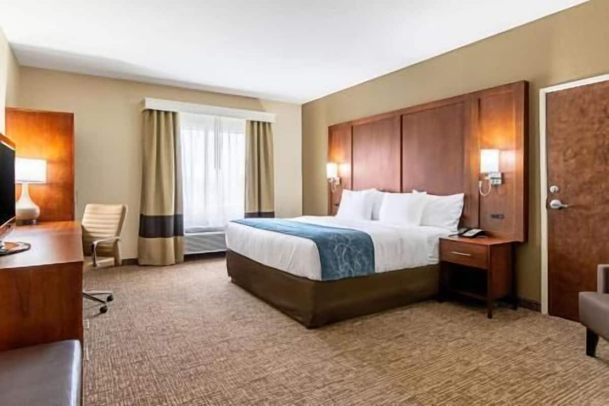 Ein Hotelzimmer mit einem großen Bett, einem Schreibtisch mit Lampe, einem Sessel und einem Kleiderschrank.